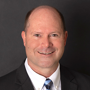 Ted Wissman, Sr. Vice President – COO, smiles in front of a black background.