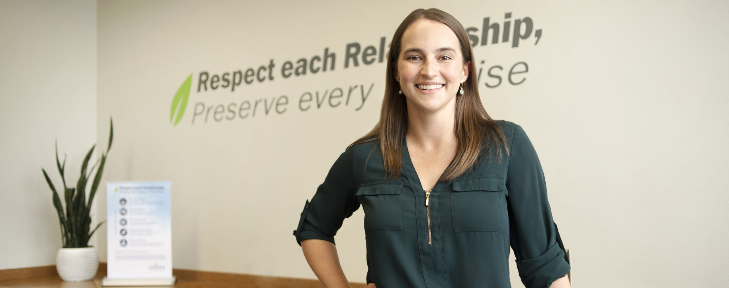 Photo of smiling female in a green shirt in front of a company branded background.
