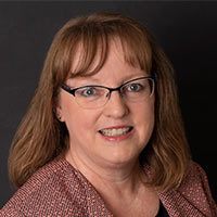 Sue Christian, Kentucky Marketing Representative, smiles in front of a black background.