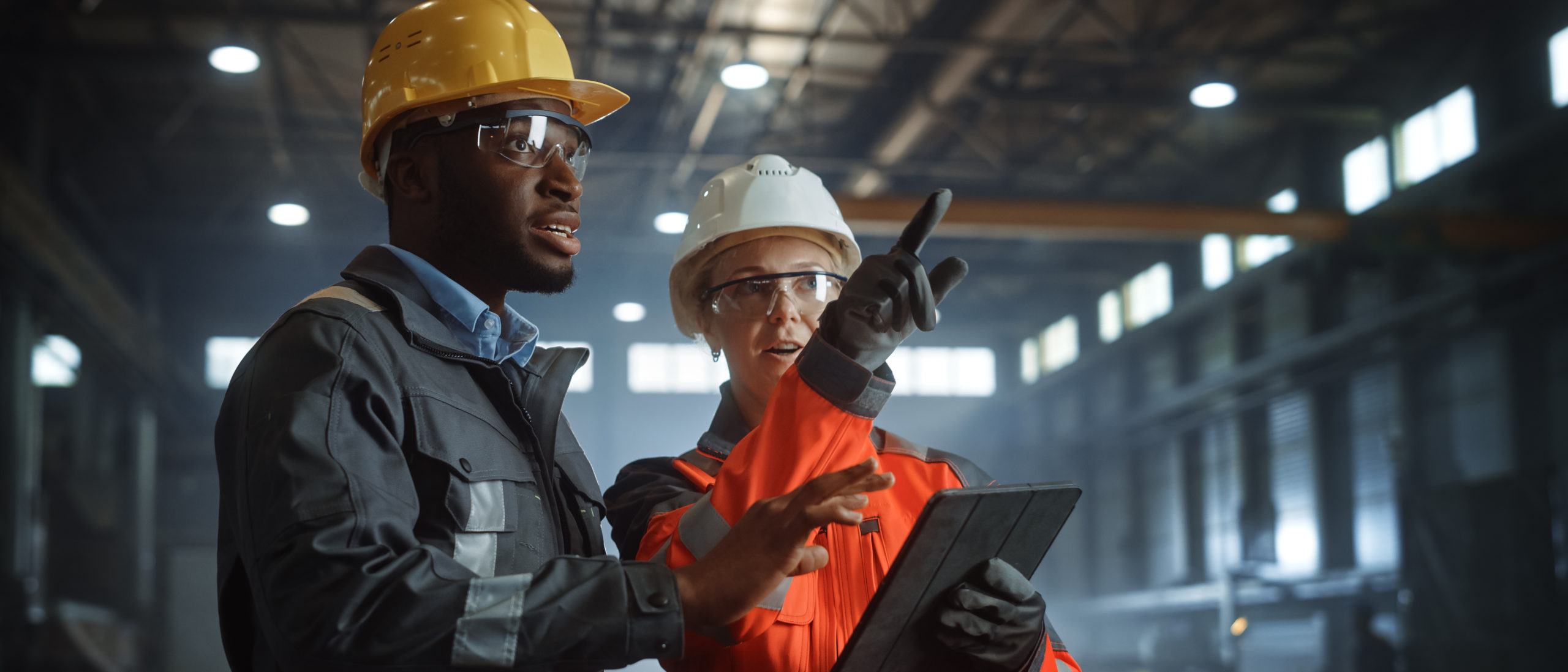 Two Heavy Industry Engineers Stand in Steel Metal Manufacturing Factory, Use Digital Tablet Computer and Have a Discussion. Black African American Industrial Specialist Talk to Female Technician.