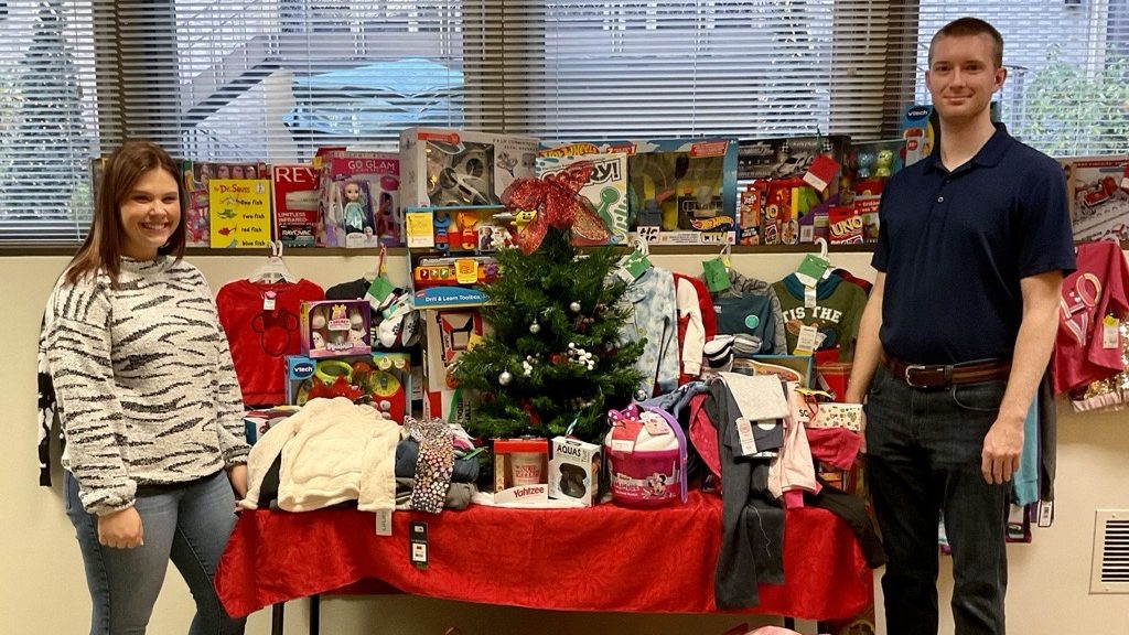 Celina Insurance Group employees Colleen Sharpin and Cole Brooks stand in front of a table full of colorful gifts bound for the Mercer County Angel Tree program.