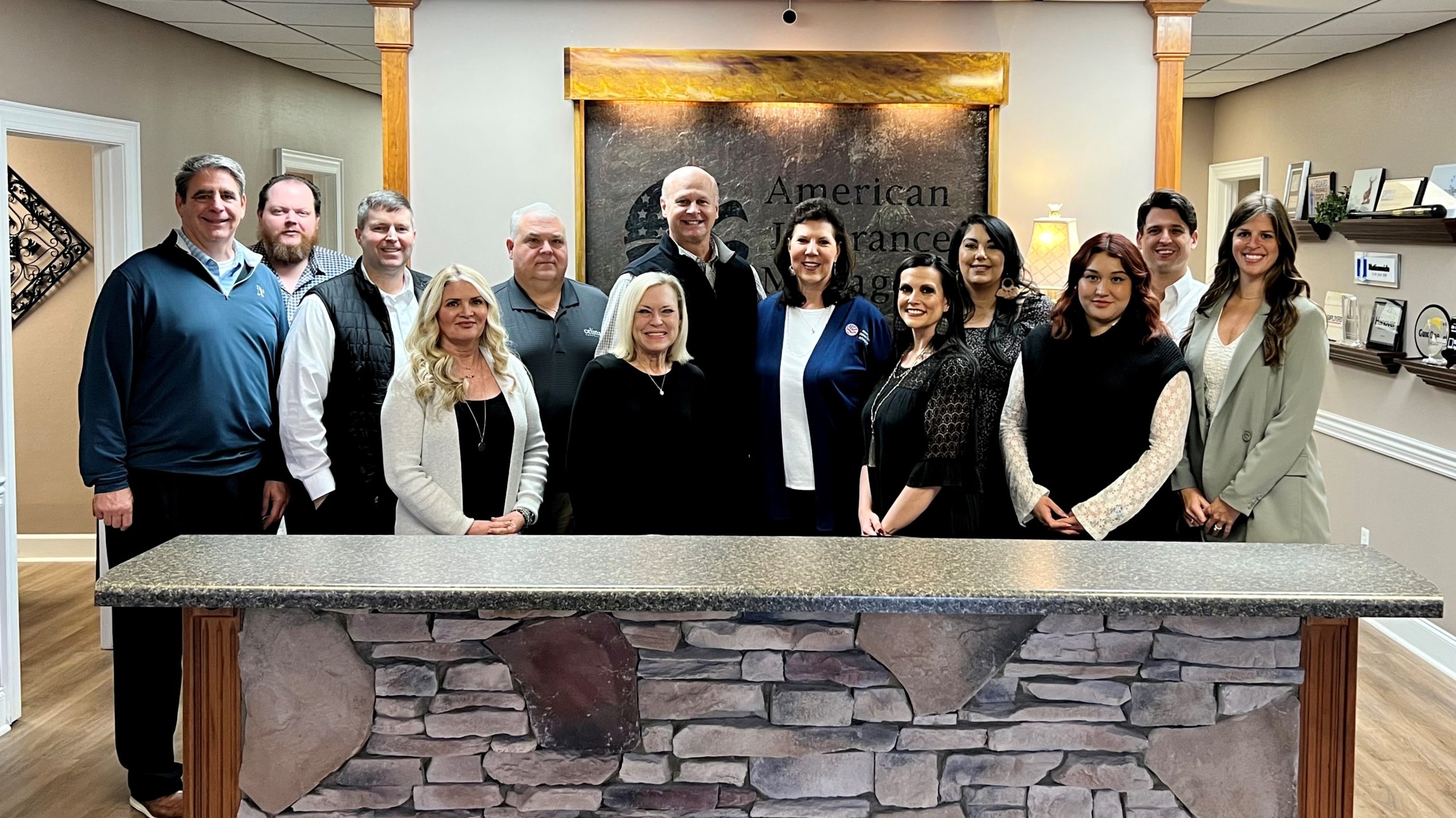 Pictured are staff members of American Insurance Managers posing for a group photo in their office behind a counter lined with stones.