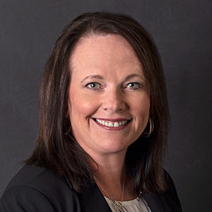 Trish Harlamert, Vice President of Underwriting, smiles in front of a black background.