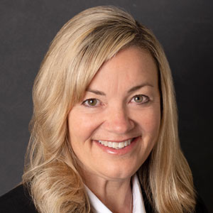 Suzanne Wells, Sr. Vice President – CFO and Treasurer, smiles in front of a black background.