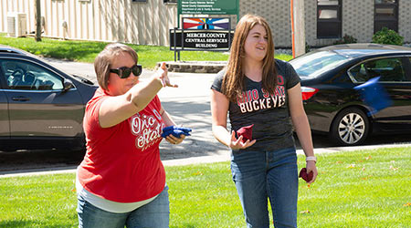 Two females in t-shirts play beanbags at a company event.
