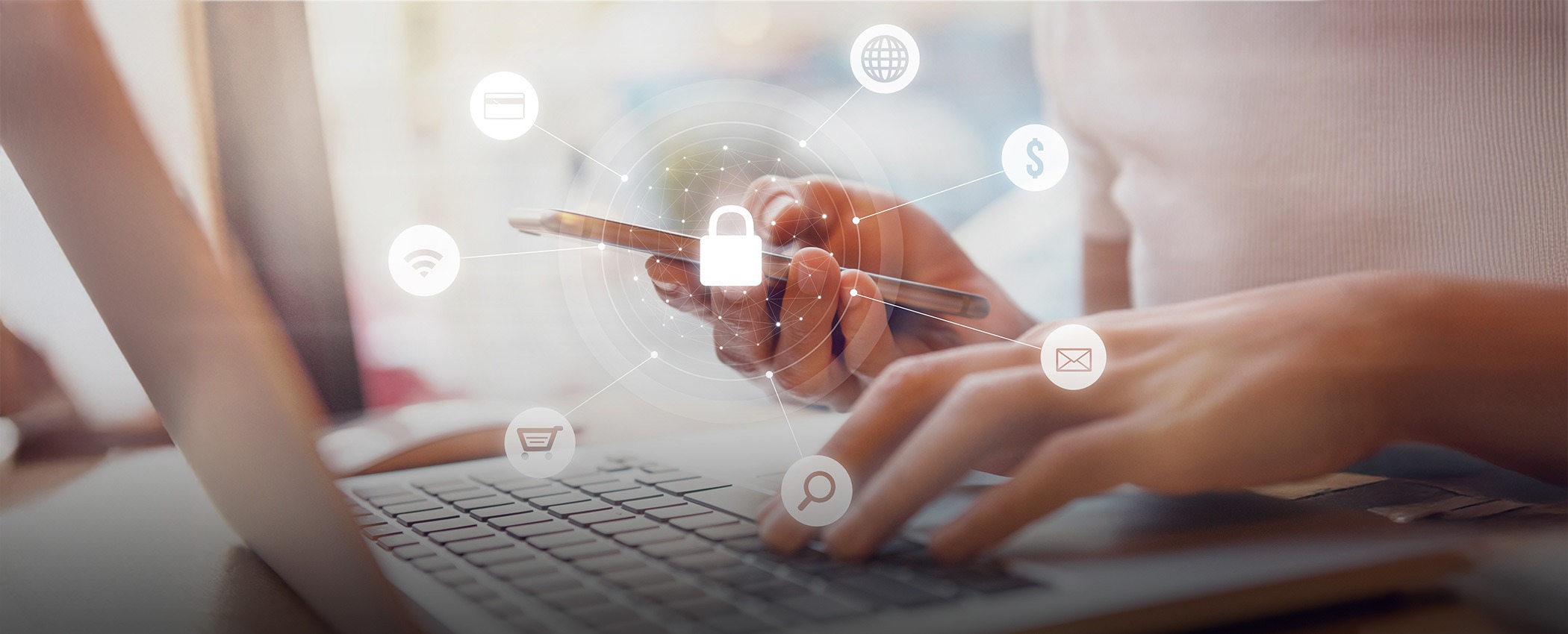 A woman works on a laptop while looking at her phone.